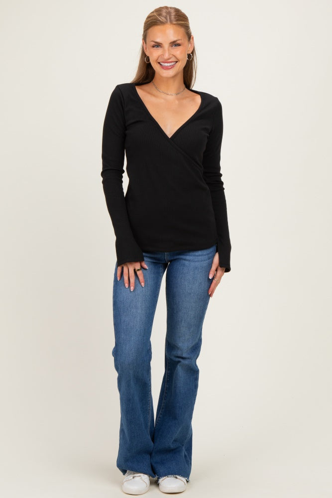 woman wearing a black long sleeve wrap top with a deep V-neck and blue flared jeans, standing and smiling