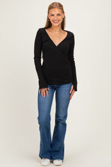 woman wearing a black long sleeve wrap top with a deep V-neck and blue flared jeans, standing and smiling