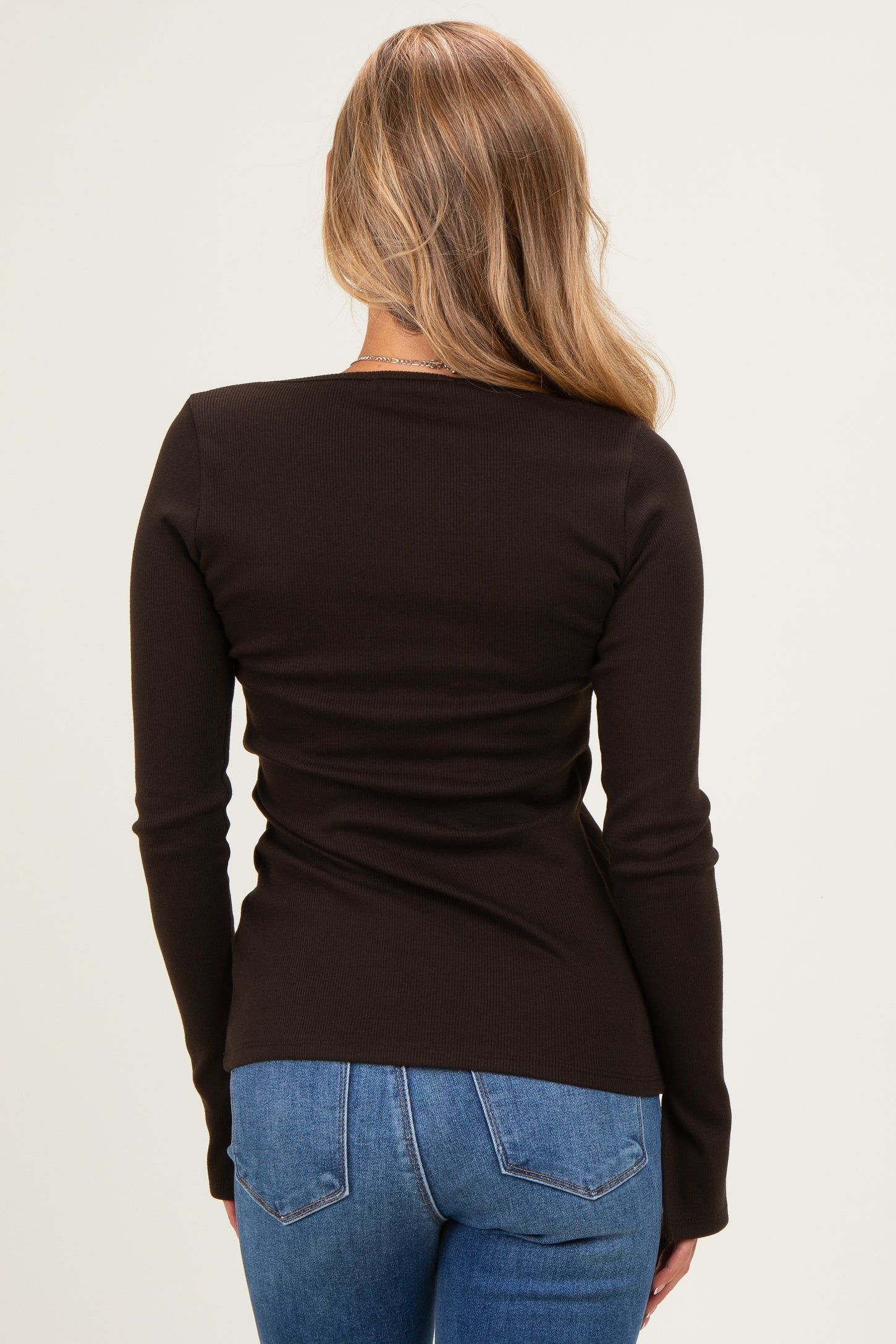 woman wearing a fitted black long sleeve top and blue jeans, viewed from the back