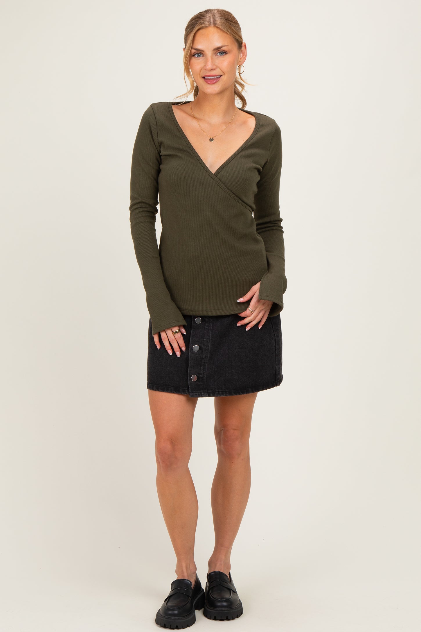 woman wearing a dark green long sleeve wrap top and a black button-front mini skirt