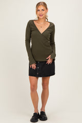 woman wearing a dark green long sleeve wrap top and a black button-front mini skirt