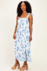 woman wearing a white floral maxi dress with blue patterns and tie straps, standing against a neutral background