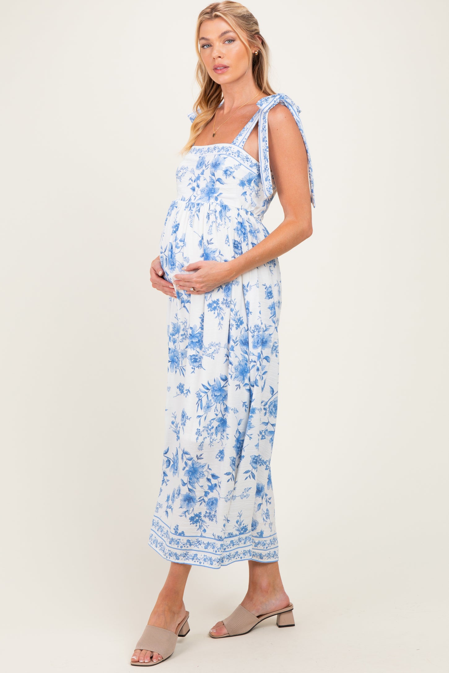 woman wearing a floral blue and white maternity maxi dress with tie straps and holding her baby bump