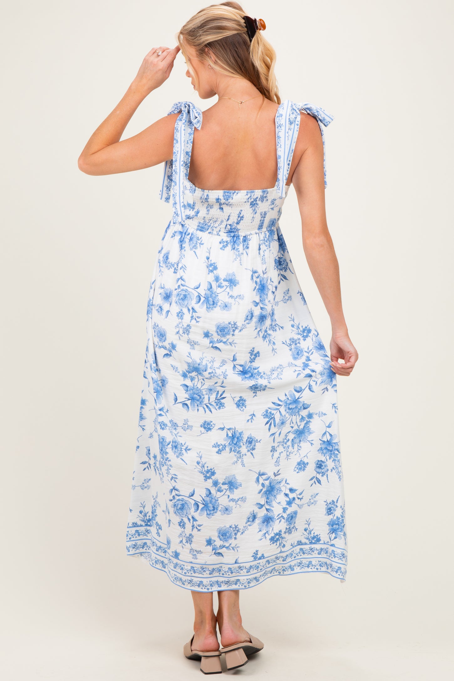 woman wearing a white floral maternity maxi dress with blue patterns and tie straps, showing her back