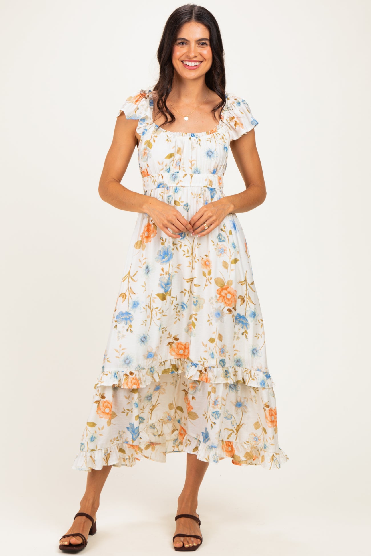 woman wearing a white floral maxi dress with ruffled sleeves and hem, standing and smiling