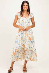 woman wearing a white floral maxi dress with ruffled sleeves and hem, standing and smiling