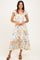 woman wearing a white floral maxi dress with ruffled sleeves and hem, standing and smiling