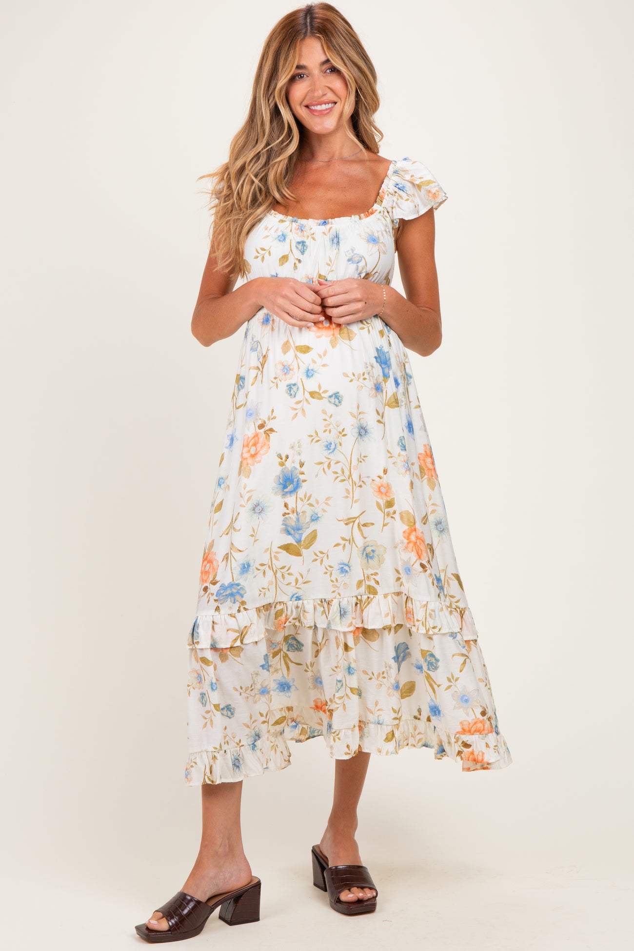 woman wearing a floral print maternity dress with ruffled sleeves and hemline, smiling against a neutral background