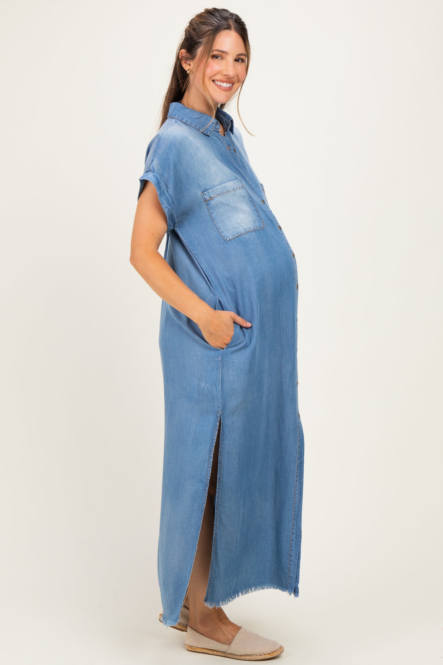 woman wearing a light blue denim maternity dress with short sleeves and pockets, showing her baby bump