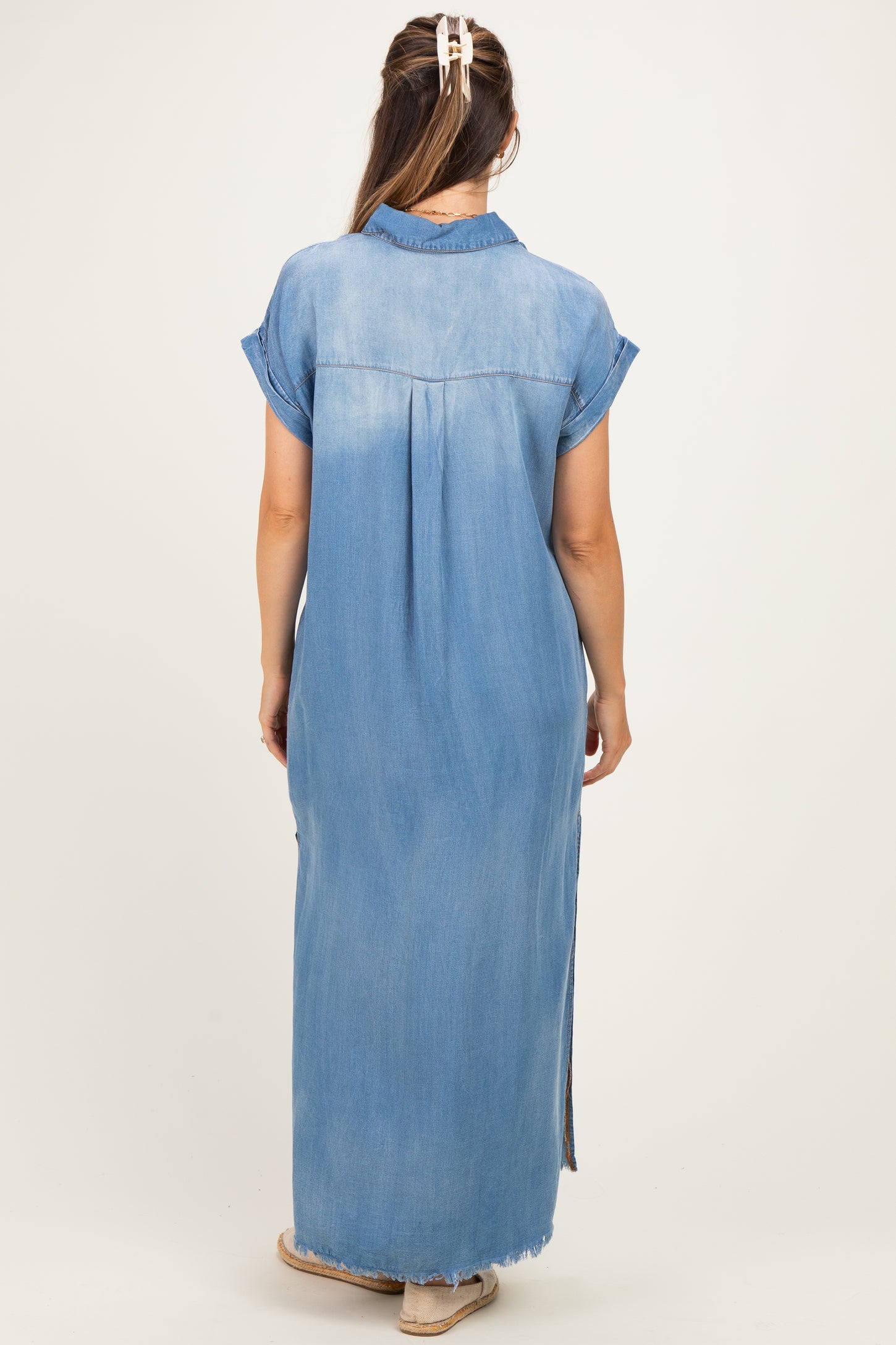 woman wearing a light blue denim maxi dress with short sleeves and side slits, showcasing her baby bump