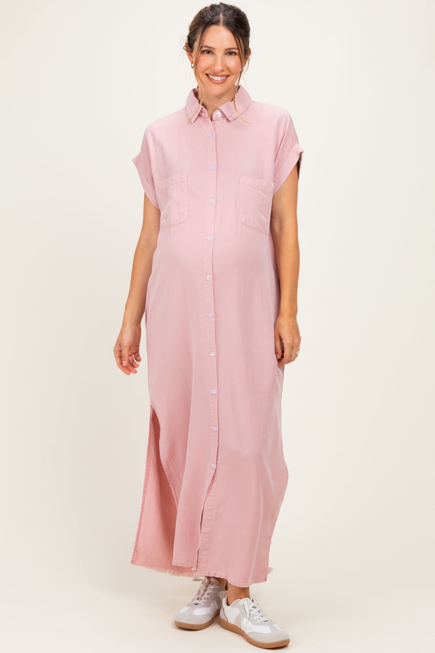 woman wearing a light pink maternity maxi shirt dress with short sleeves and side slits, showing a baby bump