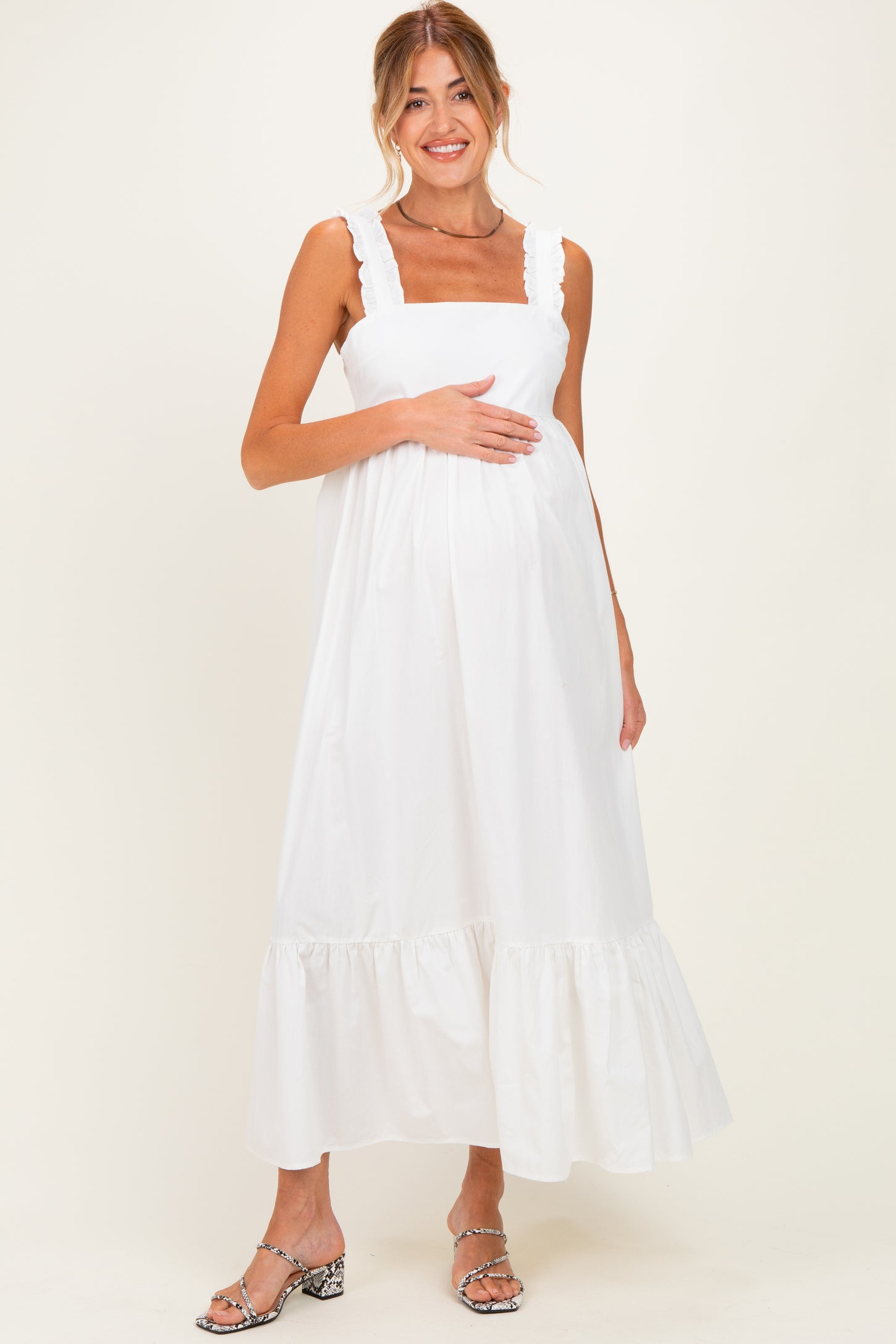 woman wearing a white maternity dress with ruffled straps and a tiered hem, holding her baby bump