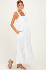 woman wearing a white maternity maxi dress with ruffled straps and pockets, displaying her baby bump