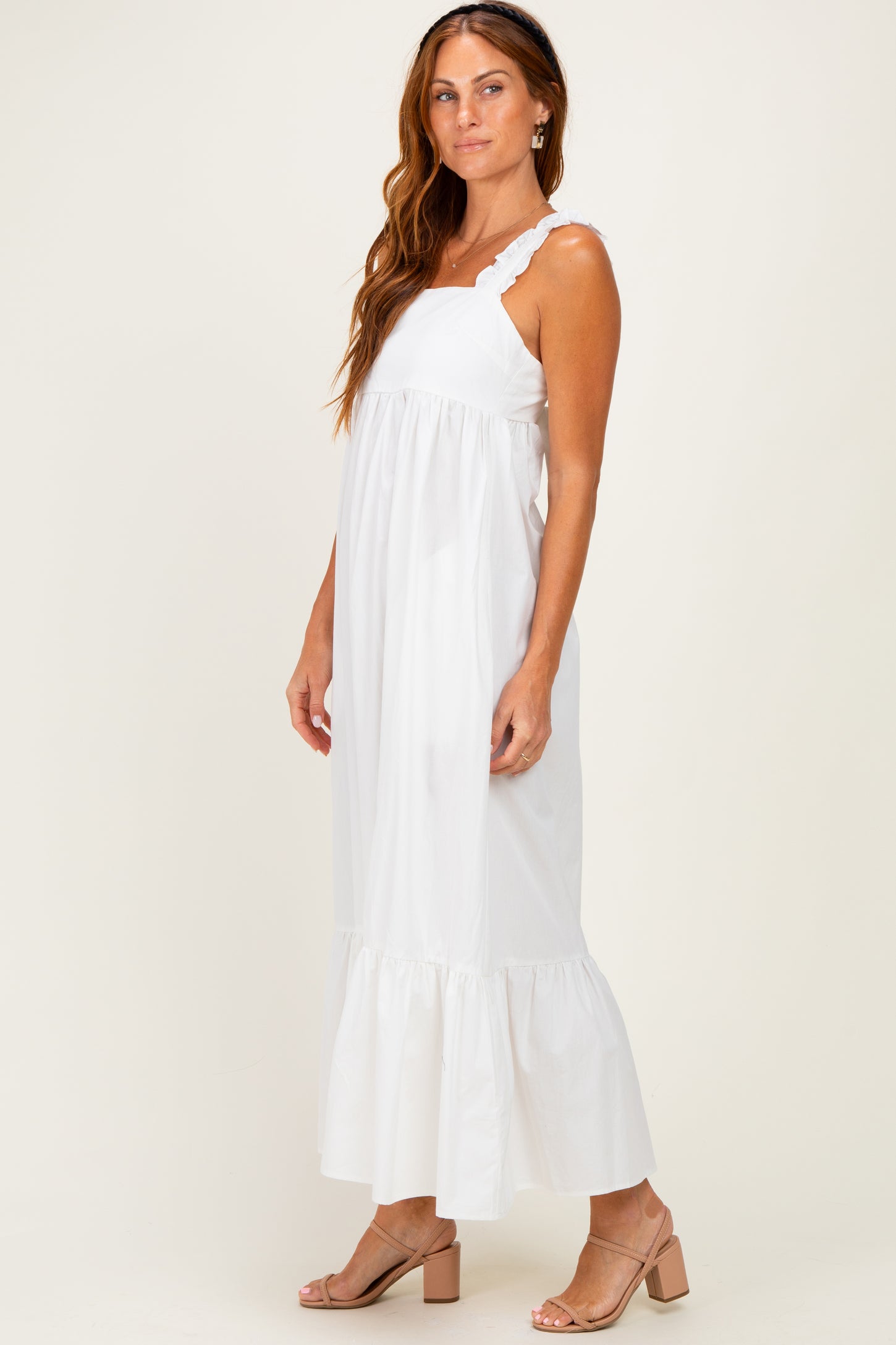 woman wearing a white maxi dress with ruffled straps and a tiered hem, standing sideways on a neutral background