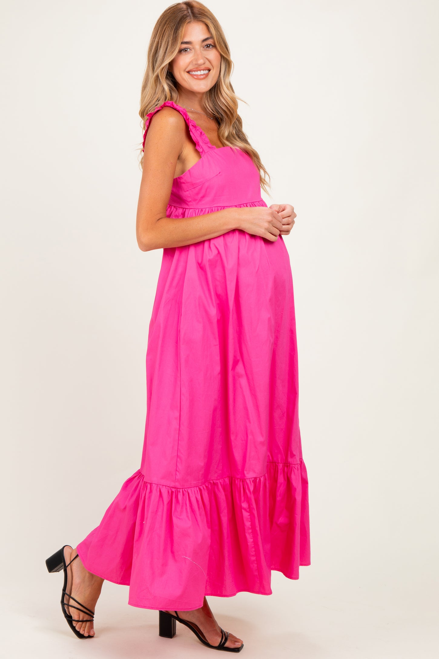 woman wearing a bright pink maternity maxi dress with ruffled straps and a tiered hem, showing her baby bump