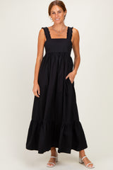 woman wearing a black maxi dress with ruffled straps and a tiered skirt.