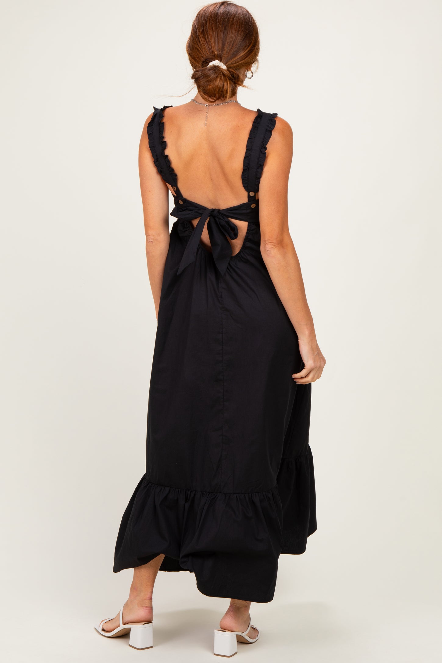 woman wearing a black maxi dress with ruffled straps and a bow detail at the back