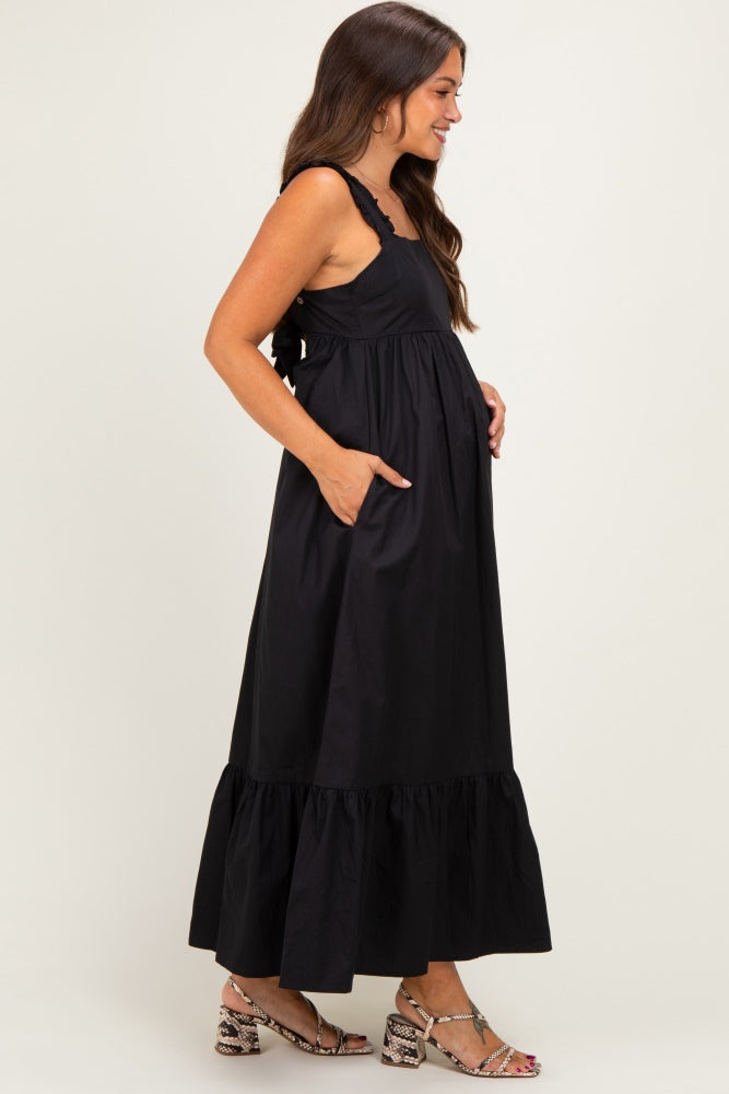 woman wearing a black maternity maxi dress with ruffle straps and pockets, showcasing her baby bump