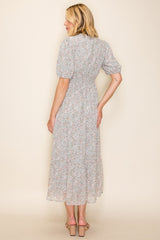 woman wearing a light floral midi dress with puff sleeves and a fitted waist, standing with her back to the camera