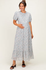 woman wearing a gray floral maternity maxi dress with puff sleeves and a gathered waist, holding her baby bump