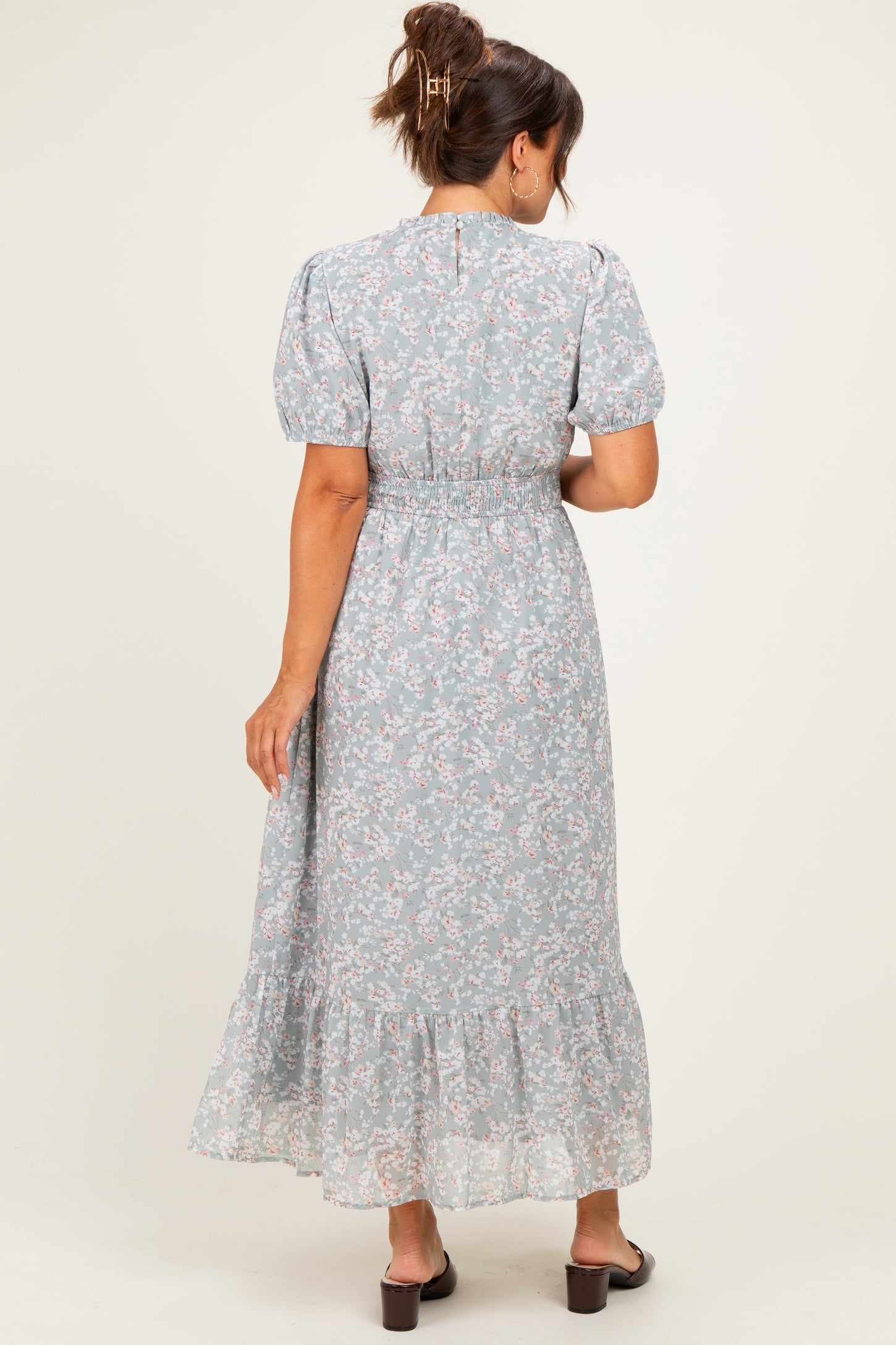 woman wearing a light blue floral maternity maxi dress with puff sleeves and a ruffled hem, showing a baby bump