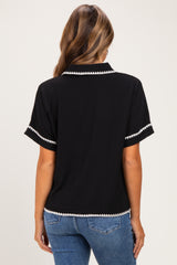 woman wearing a black short sleeve maternity top with white trim details and blue jeans
