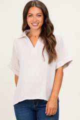 woman wearing a light pink maternity top with a collar and short sleeves, smiling at the camera