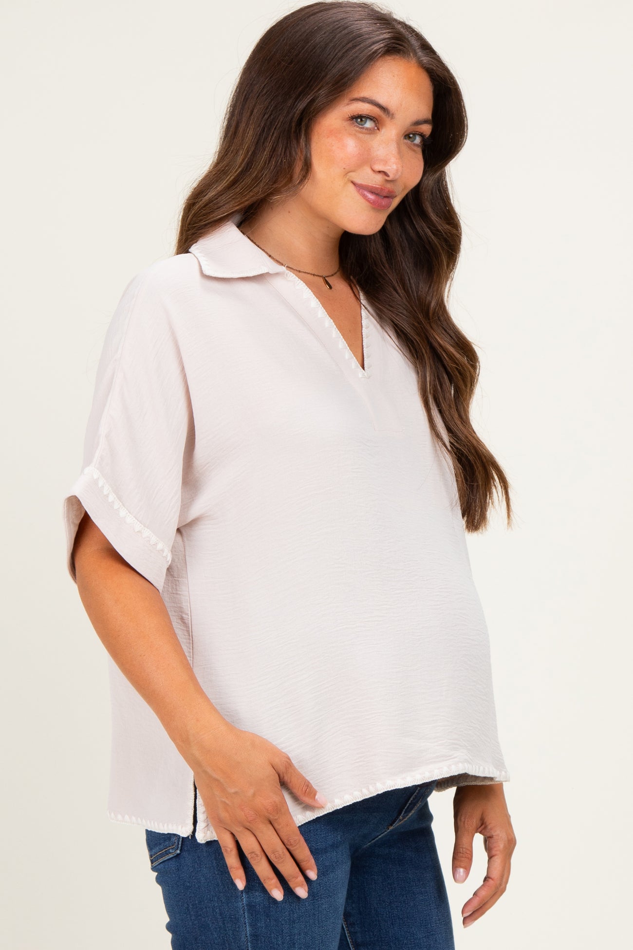 woman wearing a light pink short sleeve maternity top with a collar and side slits, showcasing her baby bump