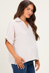 woman wearing a light pink short sleeve maternity top with a collar and side slits, showcasing her baby bump
