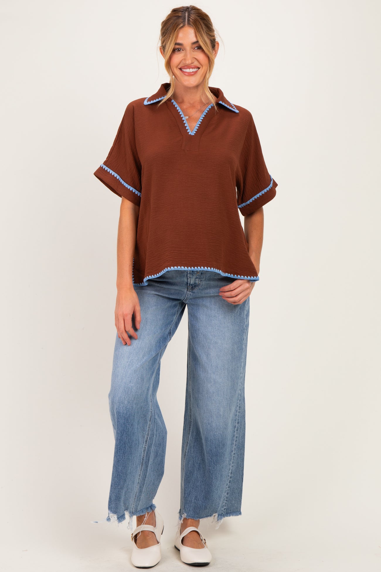 woman wearing a brown maternity top with blue trim and a relaxed fit, paired with light wash wide leg jeans