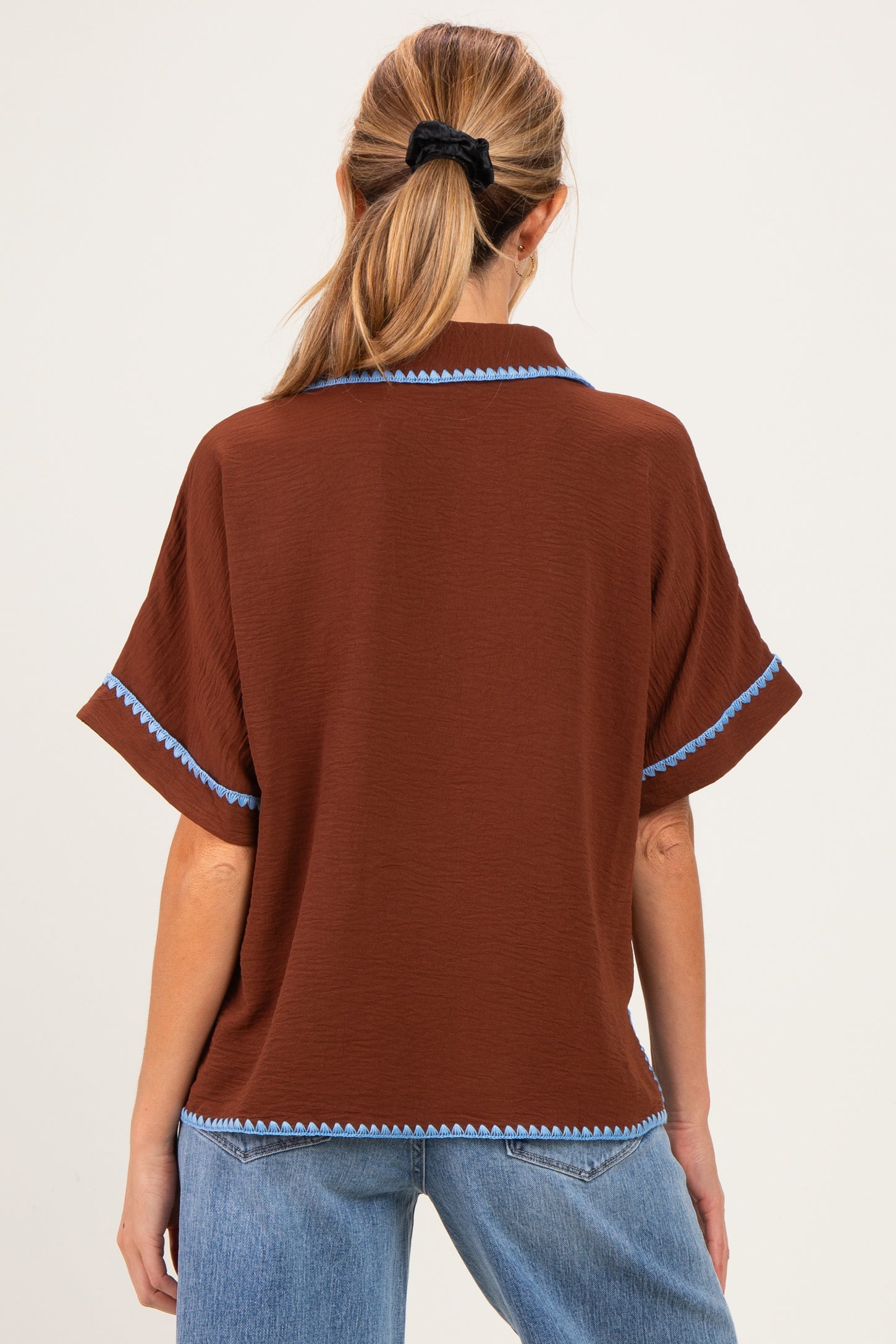 woman wearing a brown maternity top with blue trim and short sleeves, shown from the back