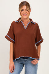 woman wearing a brown maternity top with blue trim and short sleeves, smiling against a neutral background
