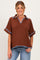 woman wearing a brown maternity top with blue trim and short sleeves, smiling against a neutral background
