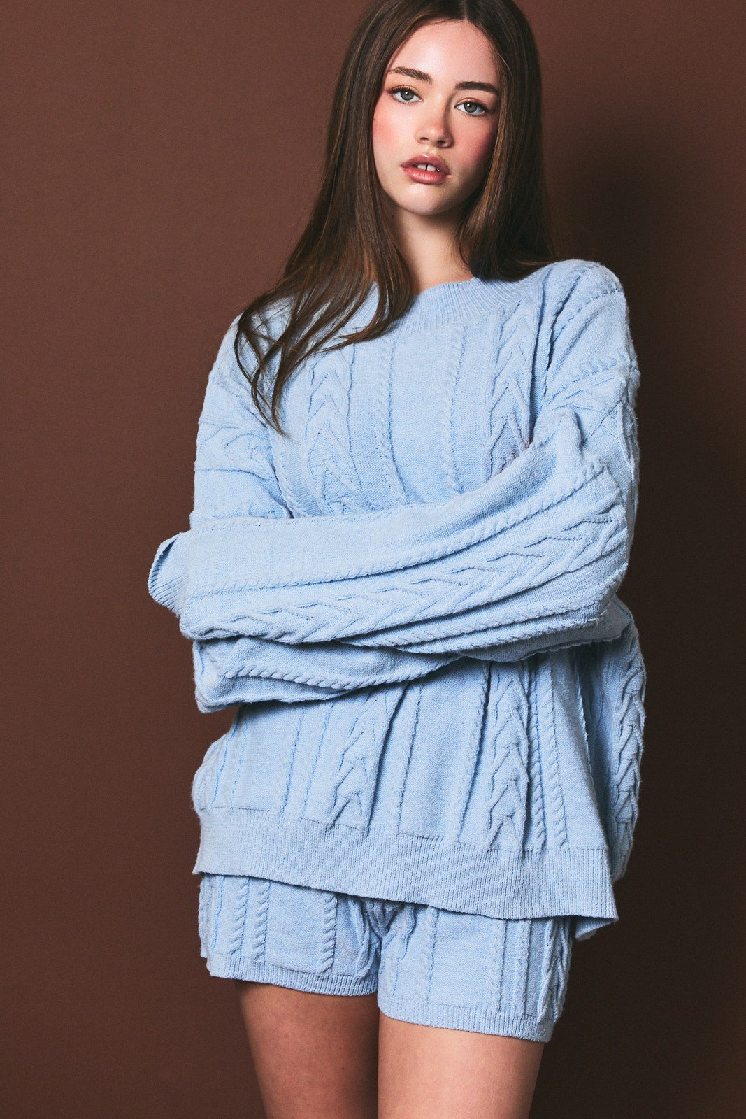 woman wearing a light blue cable knit oversized sweater and matching shorts against a brown background