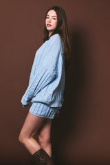 woman wearing a light blue cable knit oversized sweater and matching shorts with knee-high brown boots