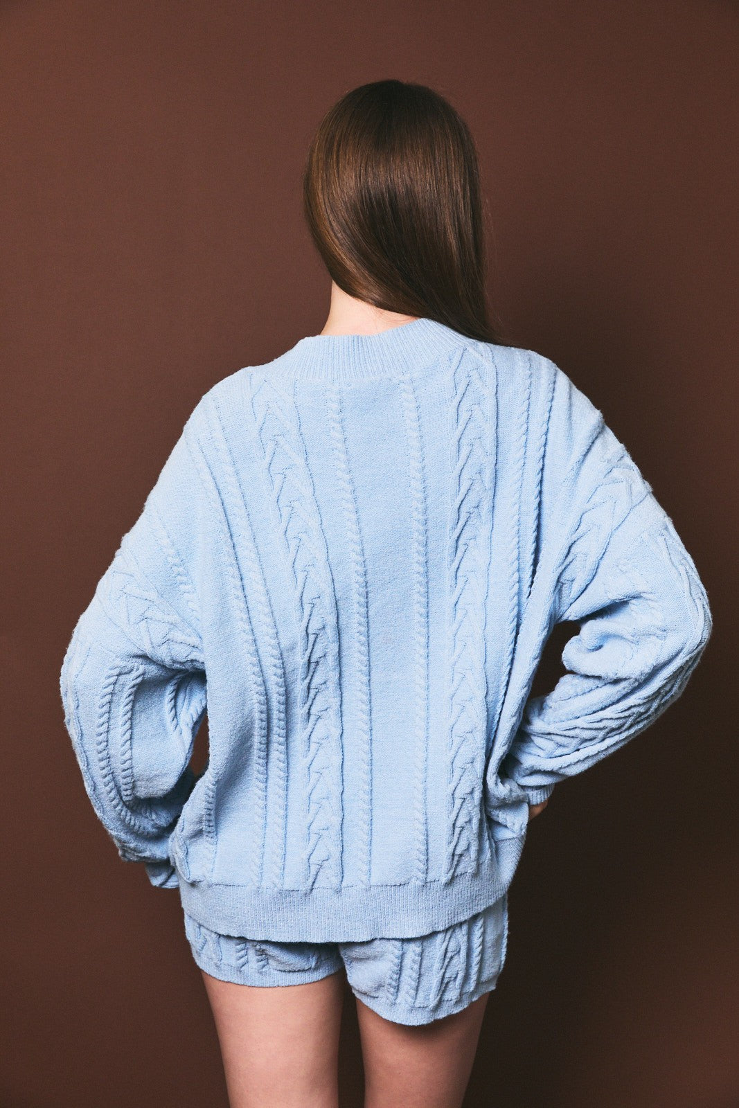 woman wearing a light blue oversized cable knit sweater and matching shorts, viewed from the back