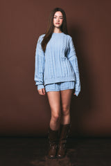 woman wearing a light blue cable knit sweater and matching shorts, paired with brown knee-high boots
