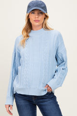 woman wearing a light blue cable knit maternity sweater with long sleeves and dark jeans