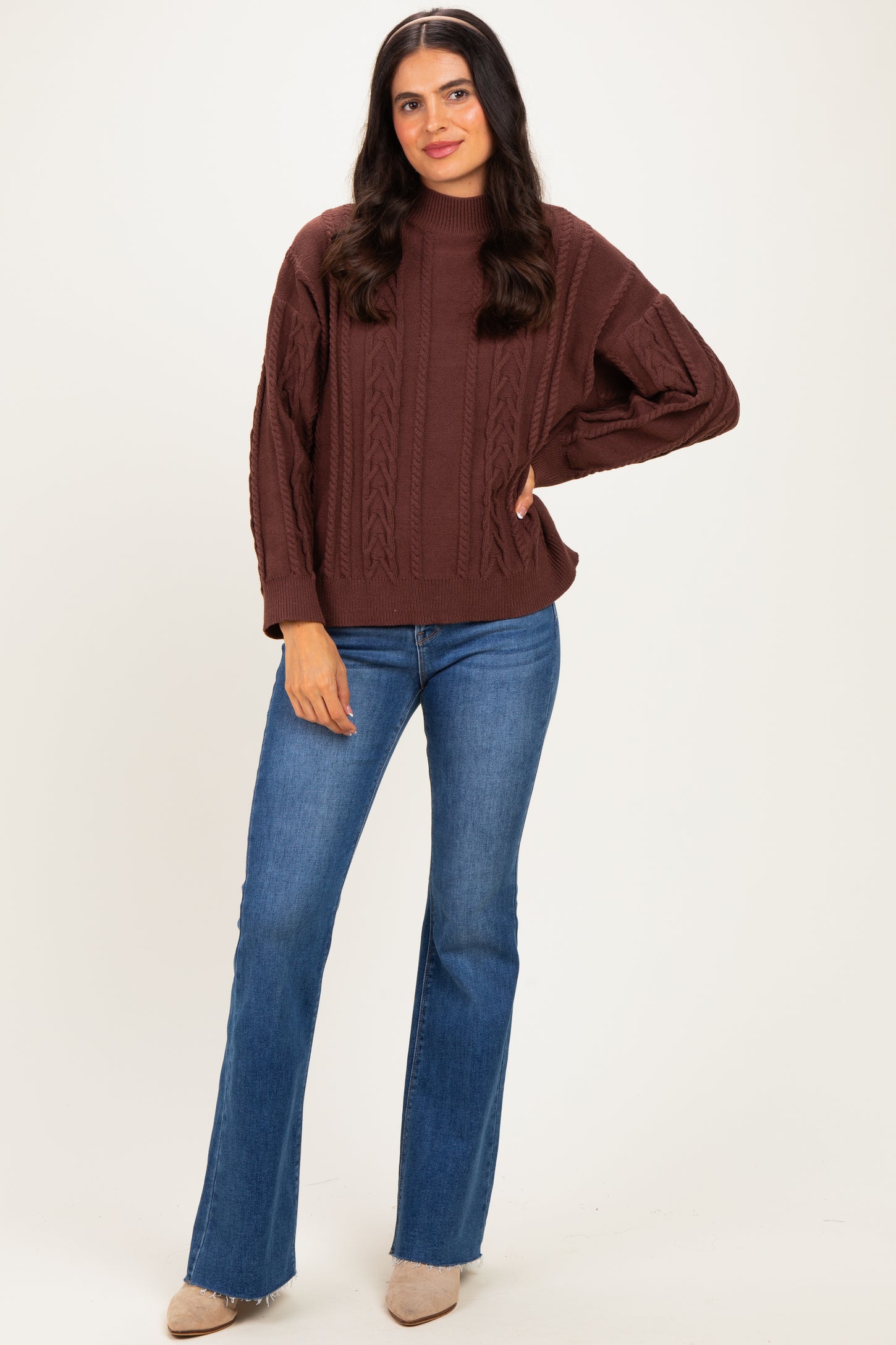 woman wearing a brown cable knit sweater and blue flared jeans, posing with one hand on her hip