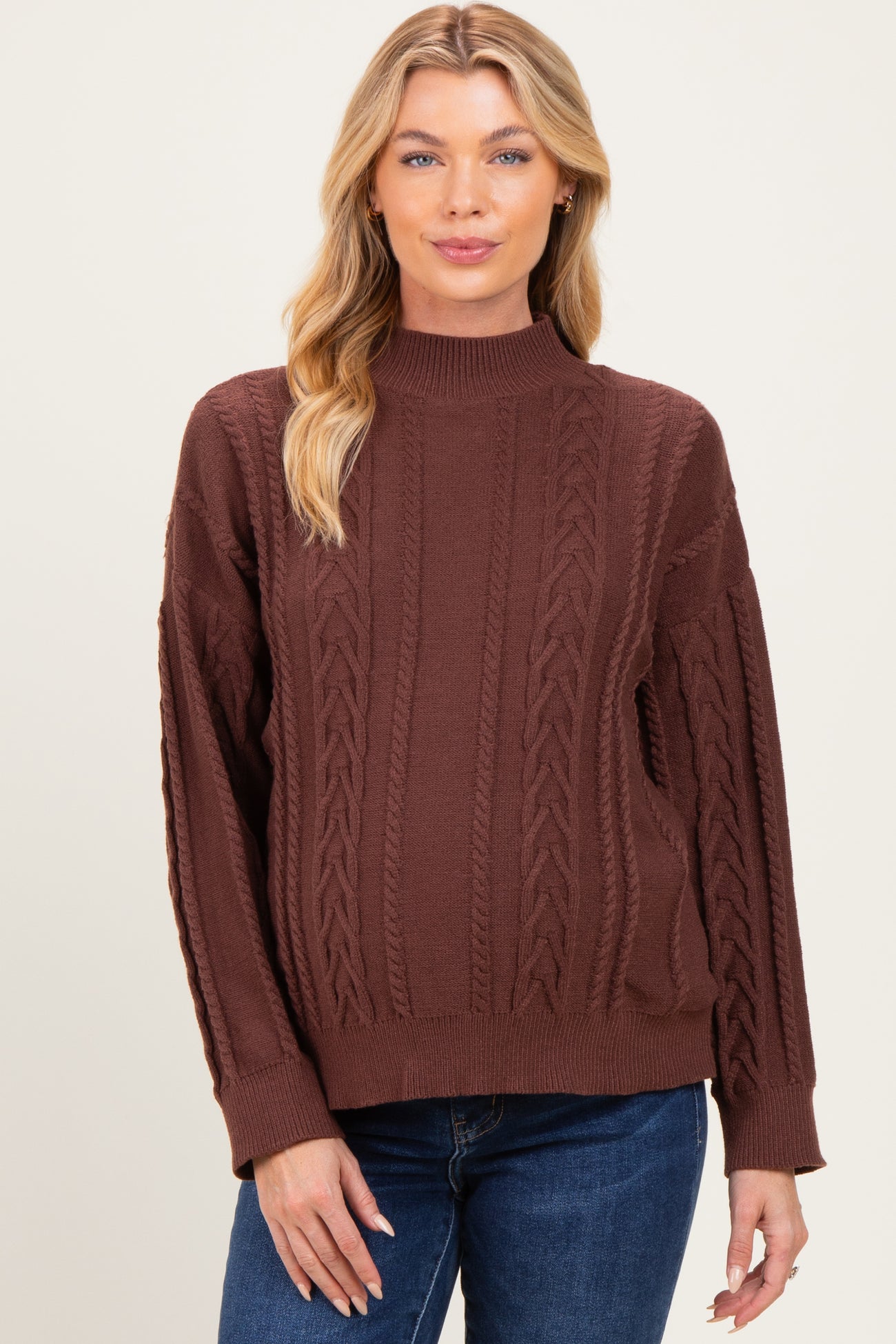 woman wearing a brown cable knit maternity sweater with a mock neck and relaxed fit, no visible baby bump