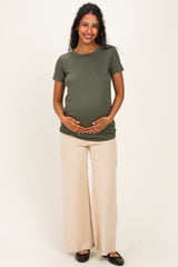 woman wearing an olive green maternity t-shirt and cream wide-leg pants, holding her baby bump