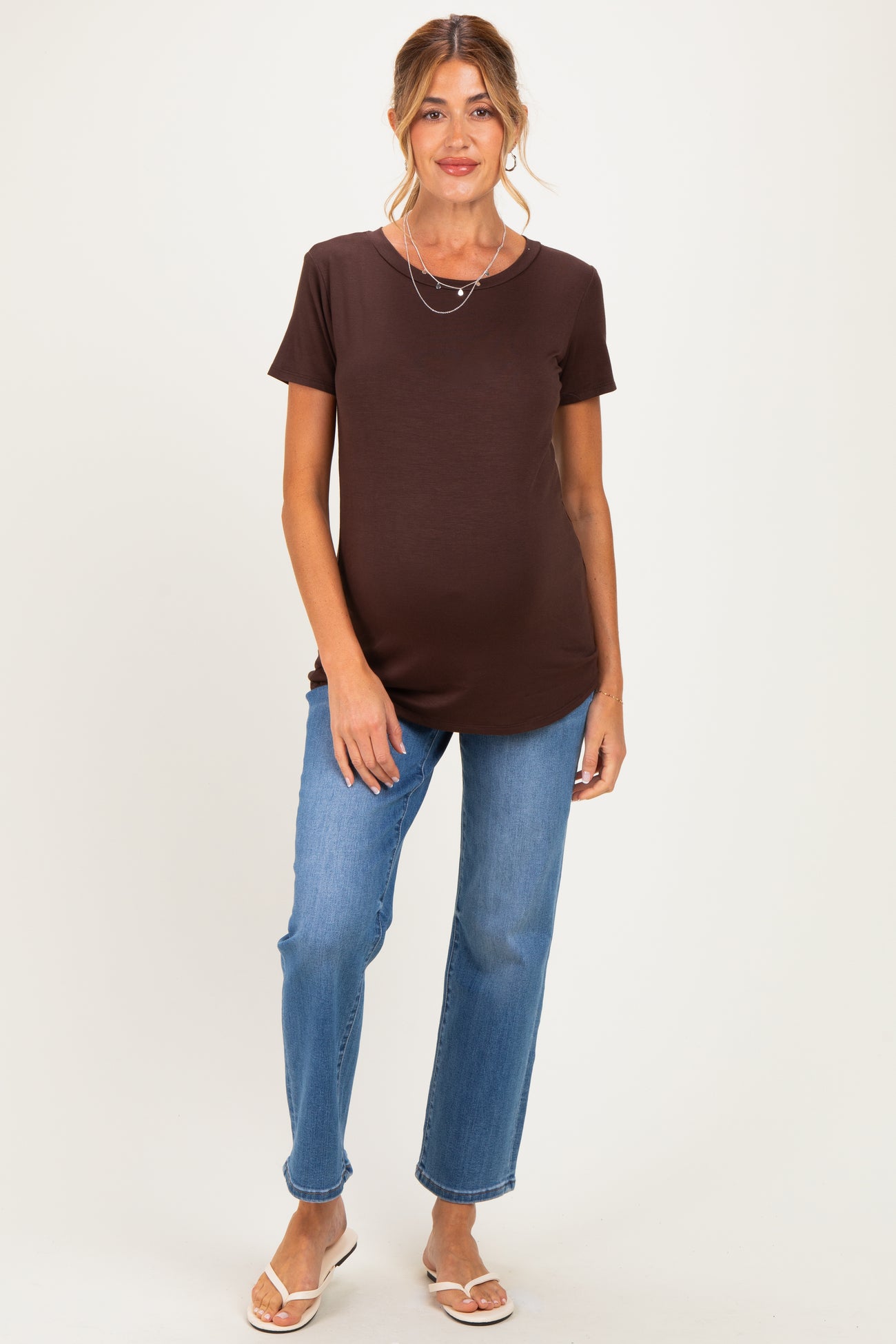 woman wearing a brown short sleeve maternity top and light blue jeans with a baby bump visible