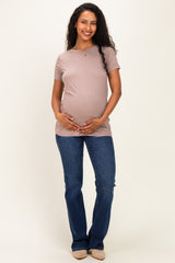 woman wearing a light brown maternity t-shirt and blue jeans, gently holding her baby bump