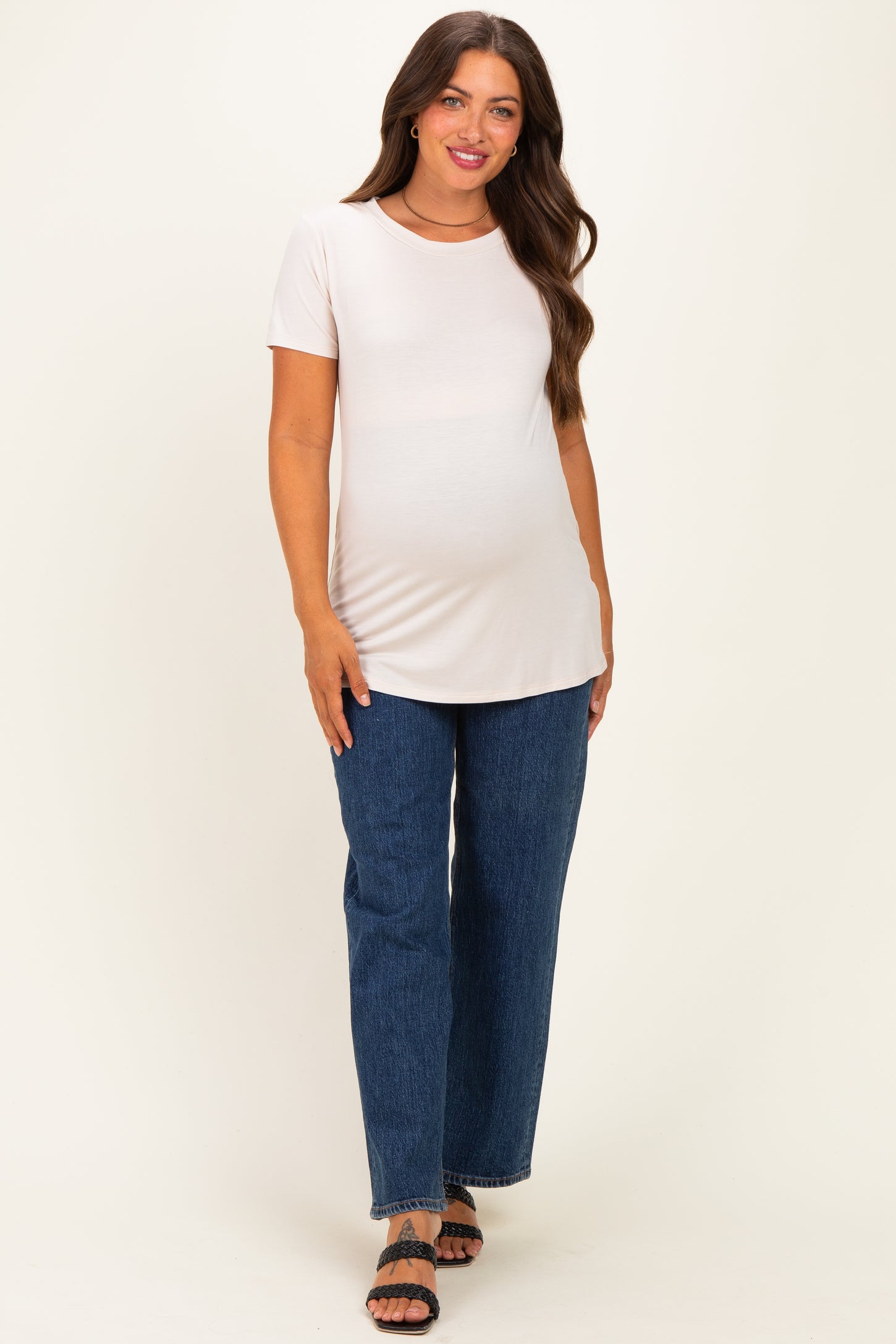 woman wearing a light pink maternity t-shirt and blue wide-leg jeans, showing a baby bump