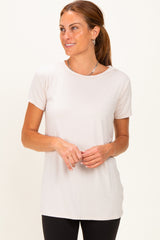 woman wearing a light beige short sleeve top with a rounded neckline and a relaxed fit, paired with black leggings