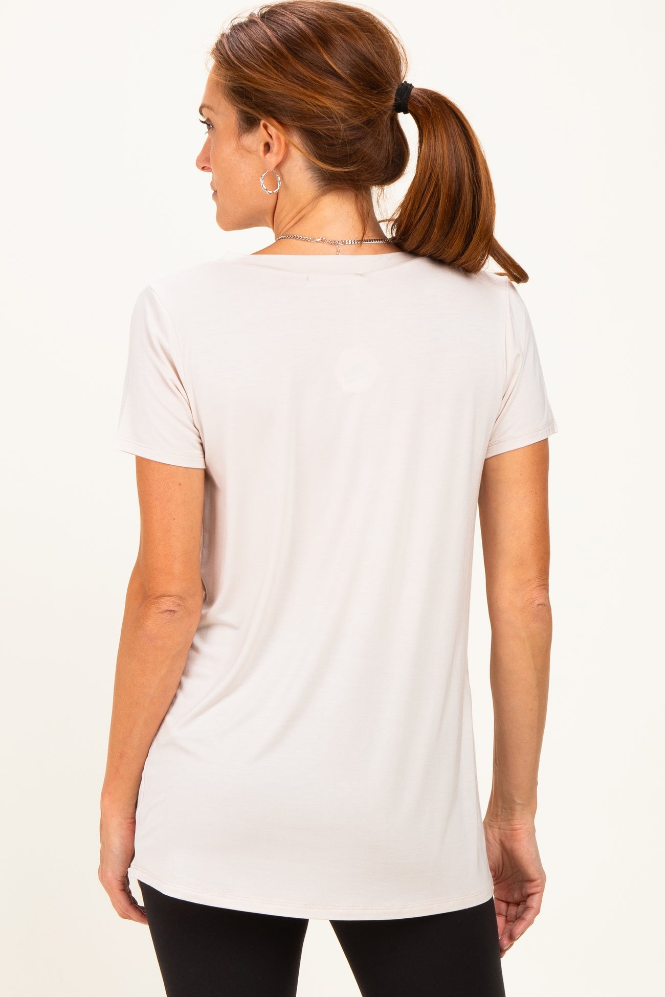 woman wearing a light beige short sleeve top with a rounded hem, shown from the back with a ponytail hairstyle