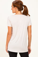 woman wearing a light beige short sleeve top with a rounded hem, shown from the back with a ponytail hairstyle