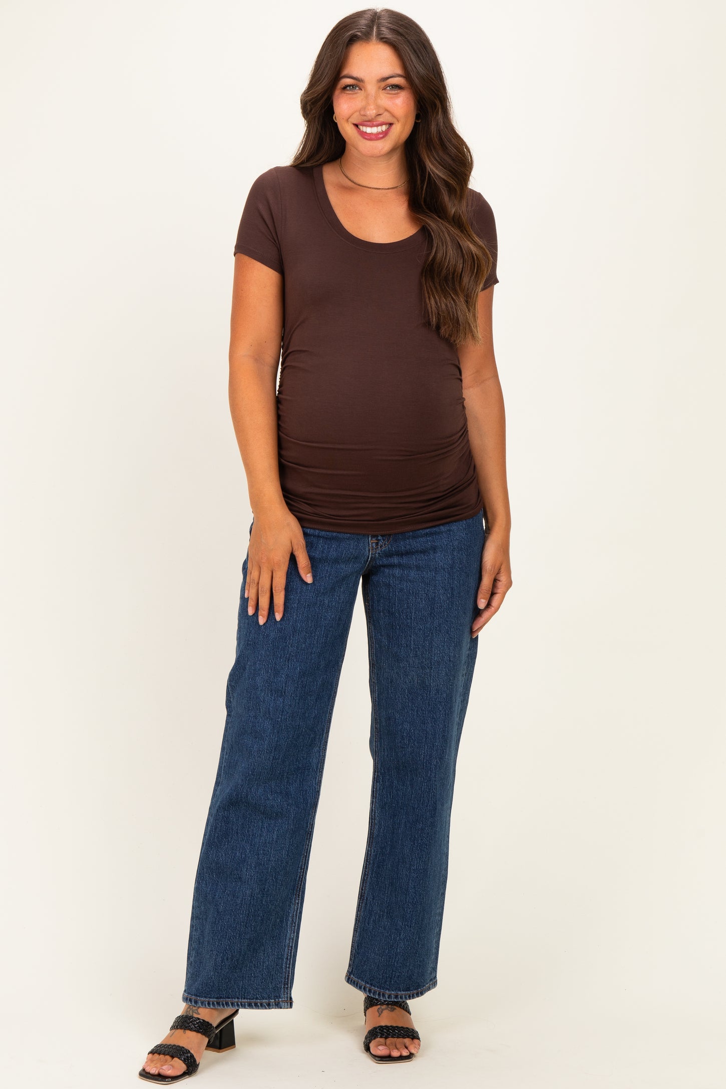 woman wearing a brown short sleeve maternity top with a ruched side and blue wide-leg jeans, showcasing her baby bump
