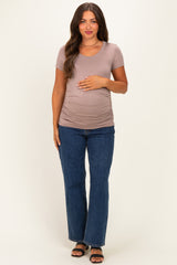 woman wearing a taupe short sleeve maternity top and blue flared jeans, gently cradling her baby bump