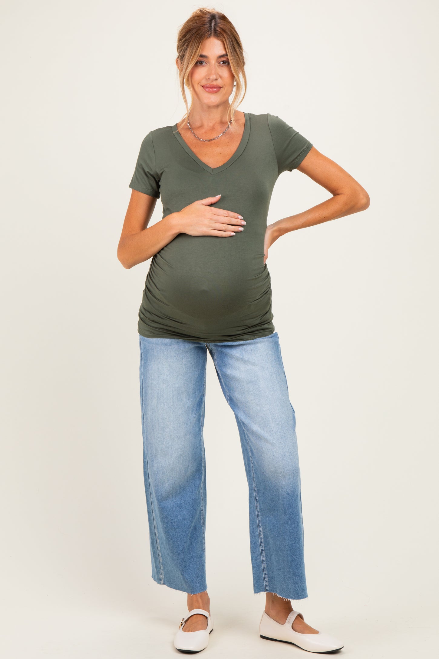 woman wearing a dark green short sleeve v-neck maternity top and jeans, holding her baby bump